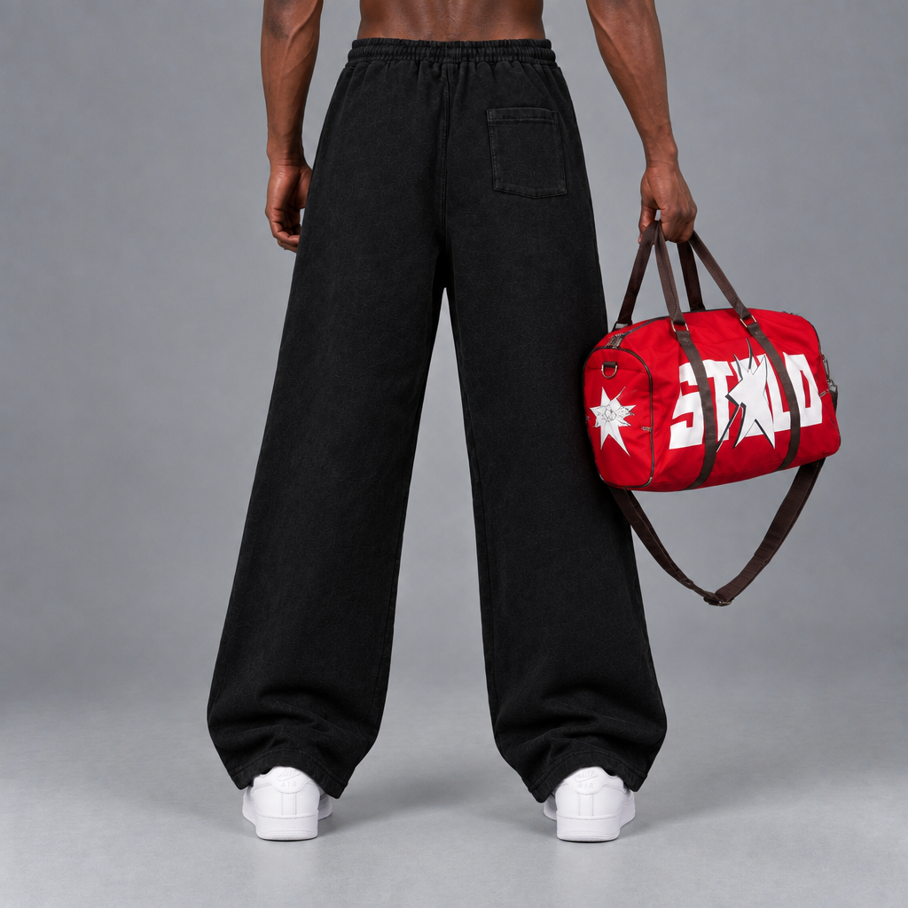 Back view of the black STOLO wide-leg pants with white Air Force Ones and the red duffle held at his side