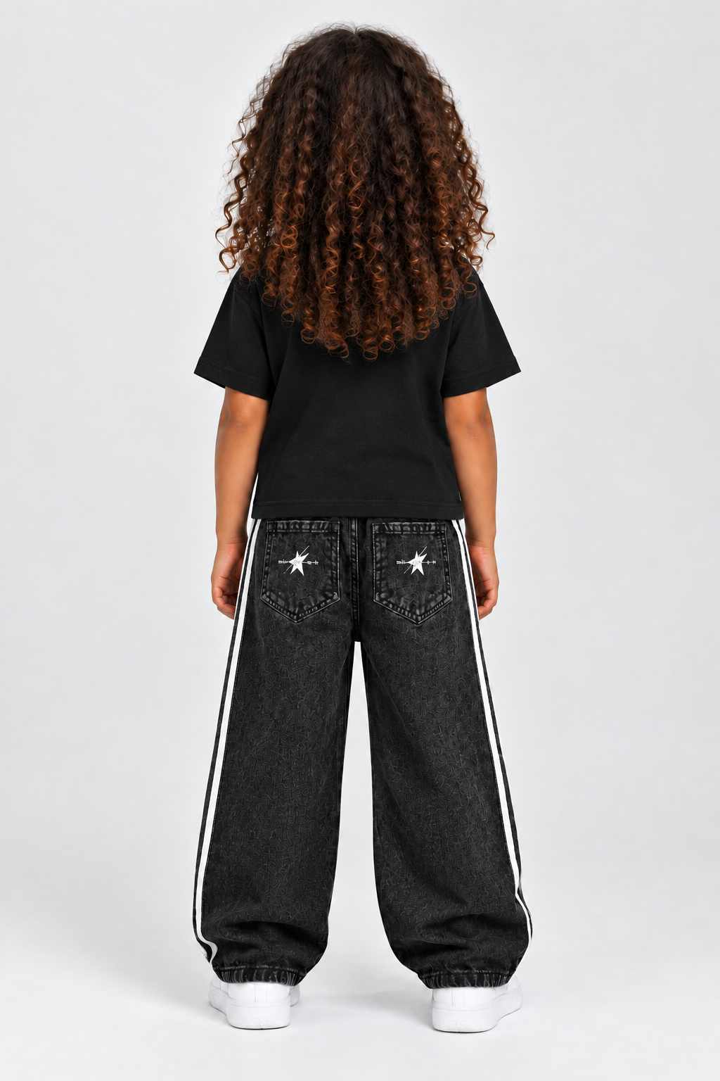 Same child model wearing the black STOLD Kids tee and striped jeans, back view