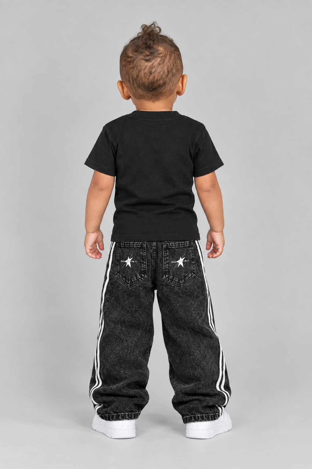 Toddler model in the black STOLD Kids tee and striped jeans, back view